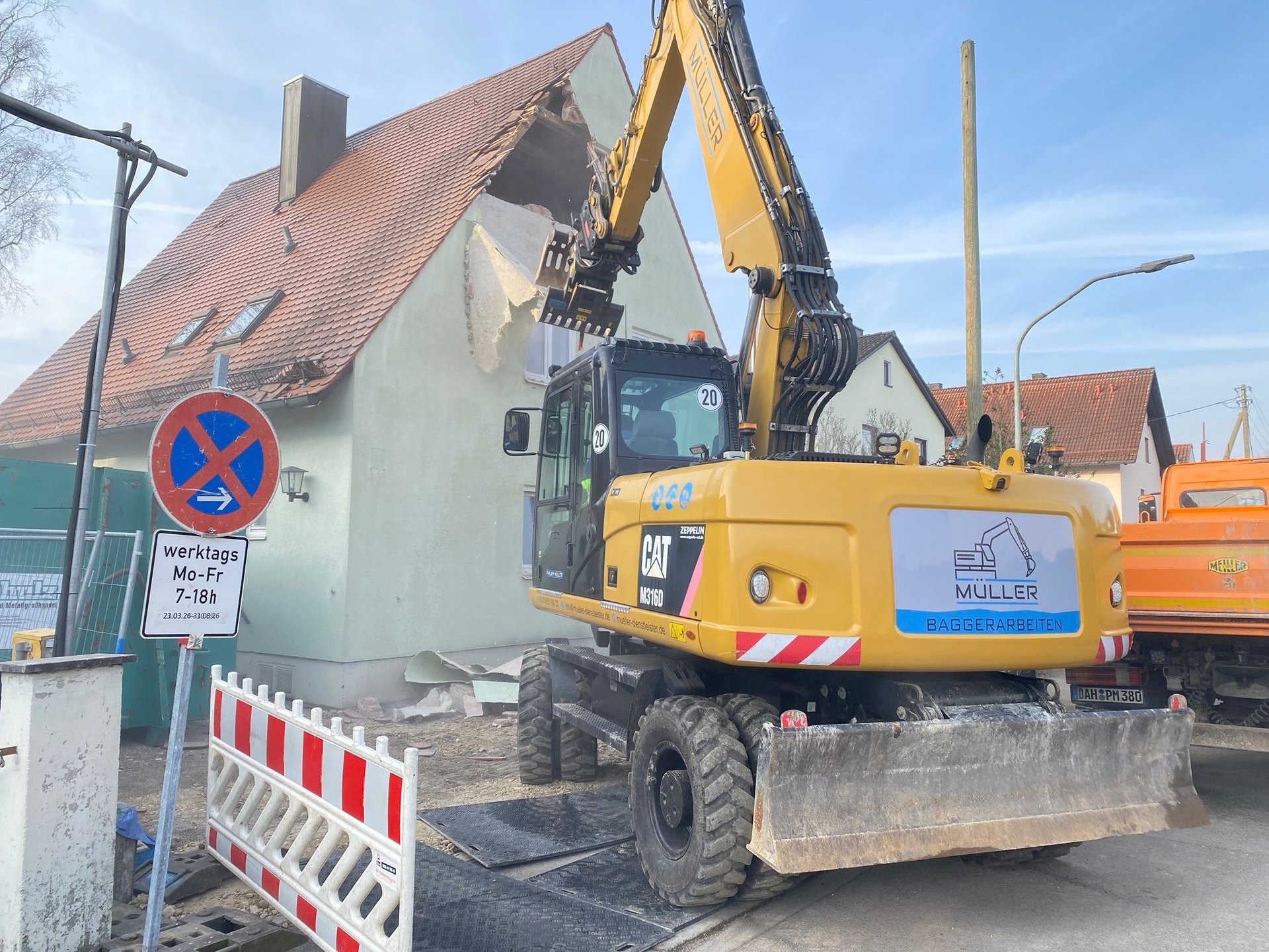 Yellow excavator demolishing a residential house with red tile roof in urban area