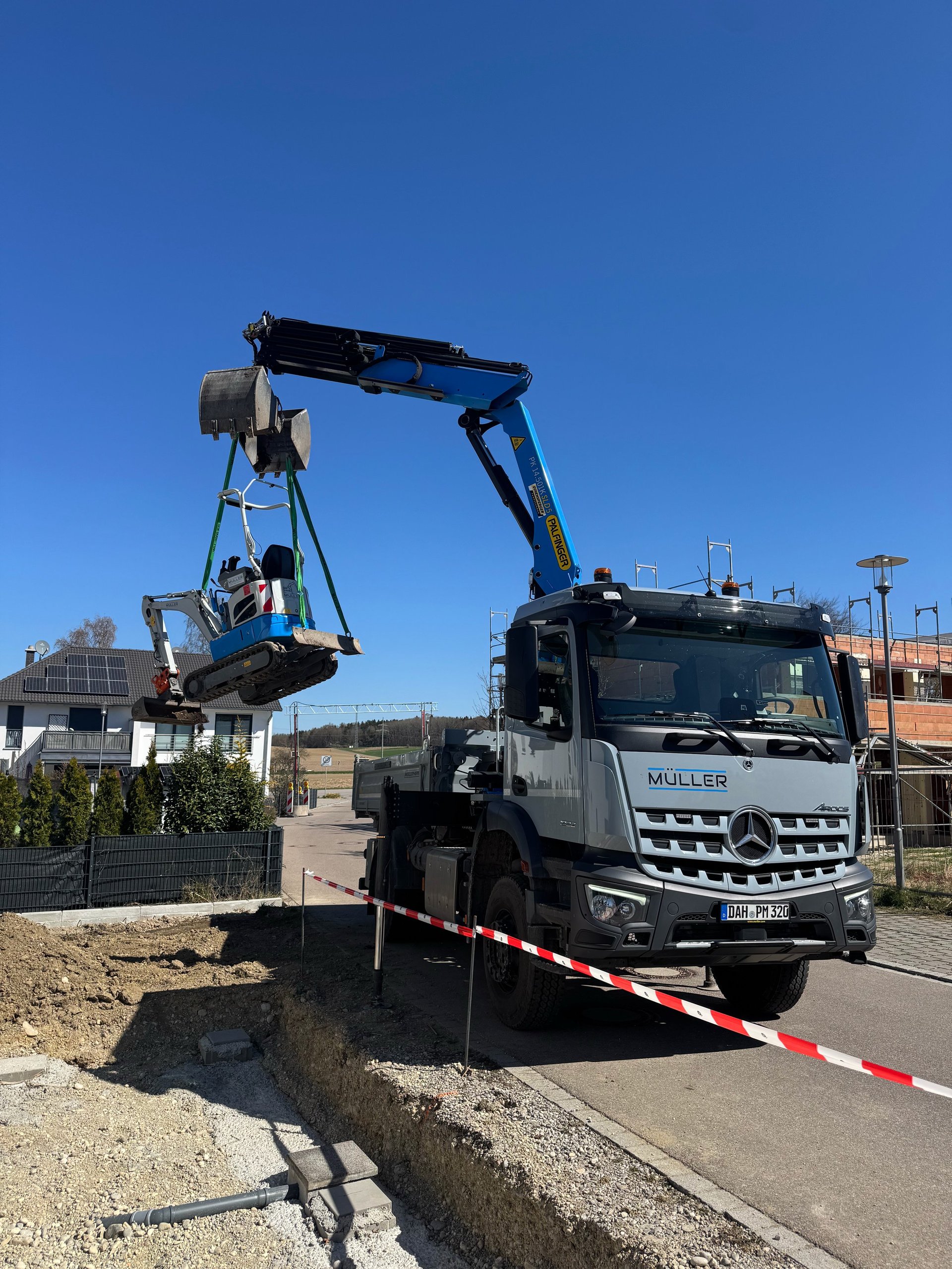 Mercedes truck with articulated arm crane loading construction equipment near a trench on a sunny day