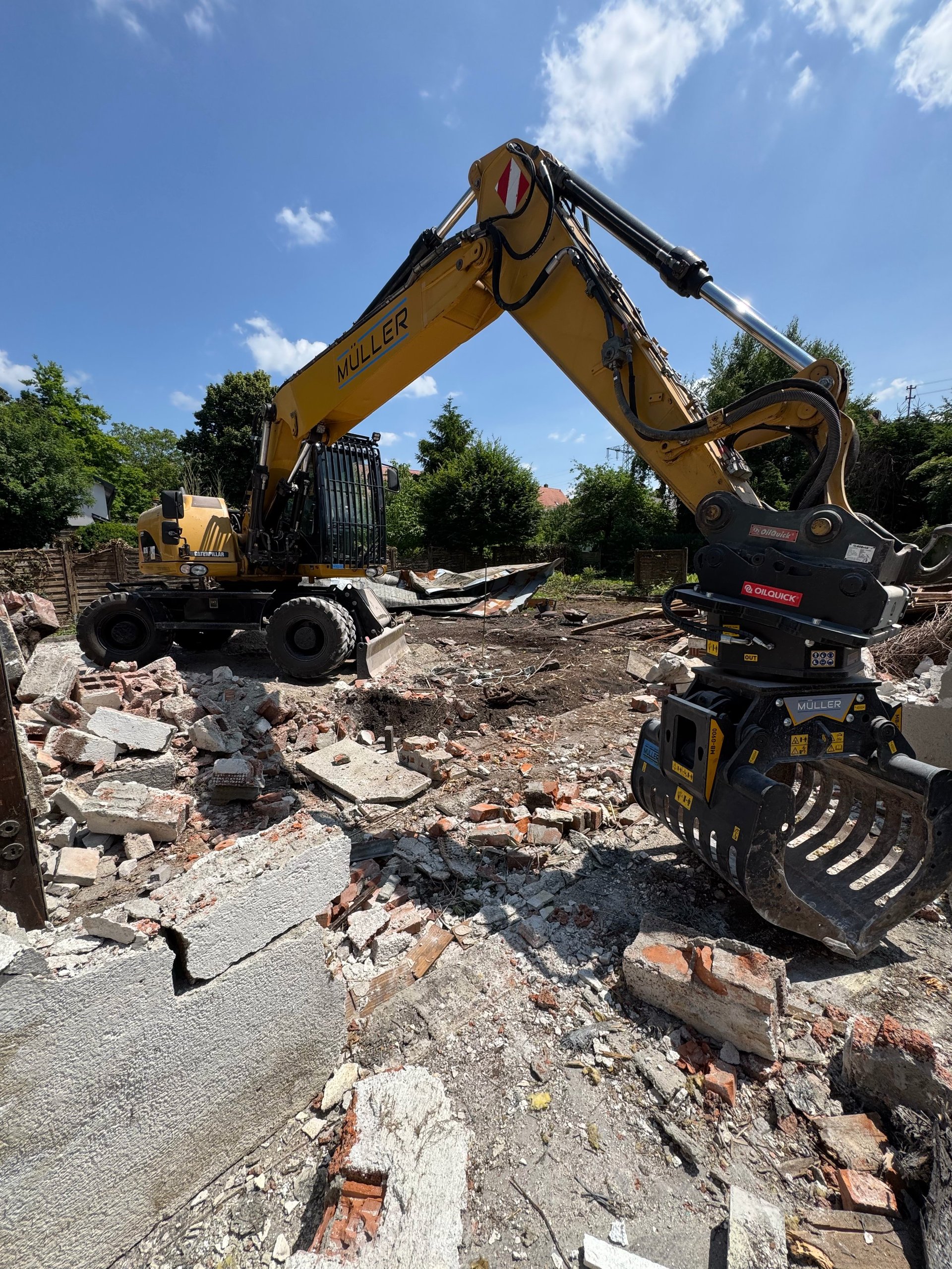Yellow excavator with grabber attachment on demolition site surrounded by rubble and debris
