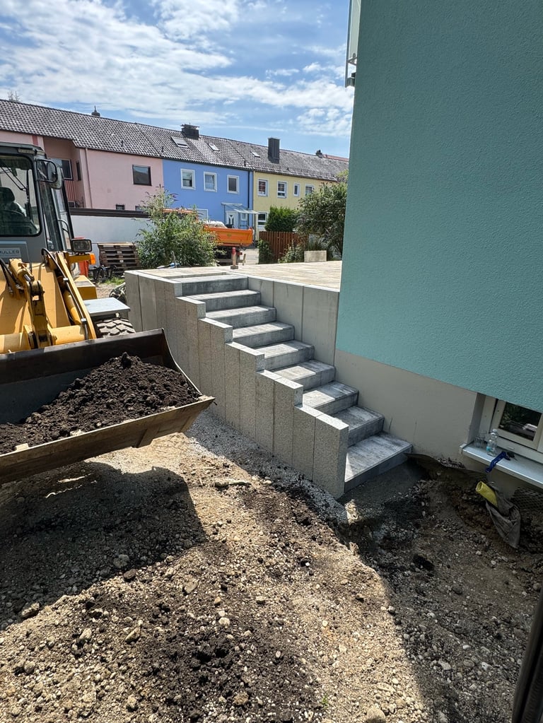 Construction site with concrete stairs leading to a blue-green building entrance, yellow excavator, and colorful residential buildings in background