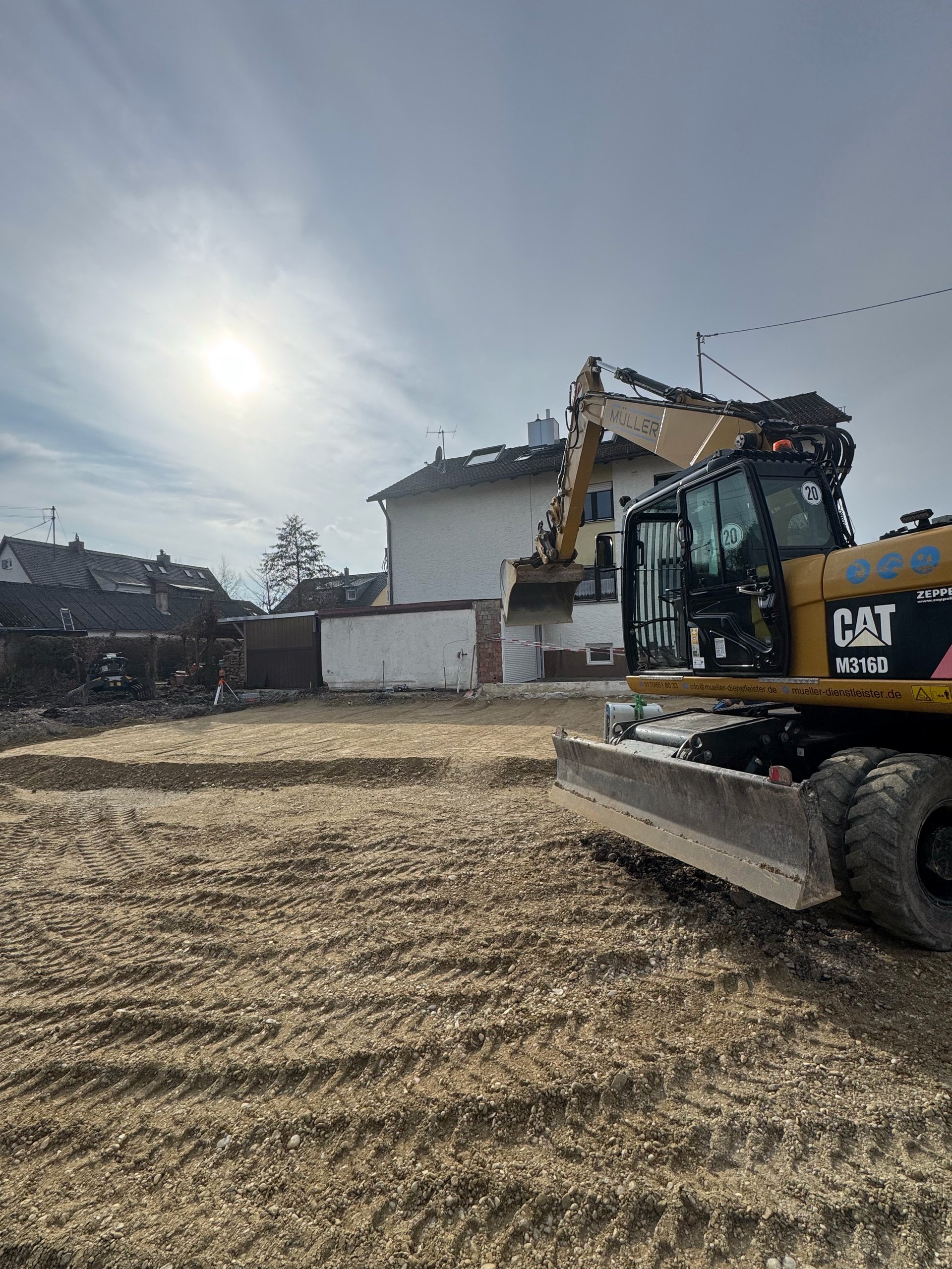 CAT excavator on construction site with residential house and cleared ground under blue sky