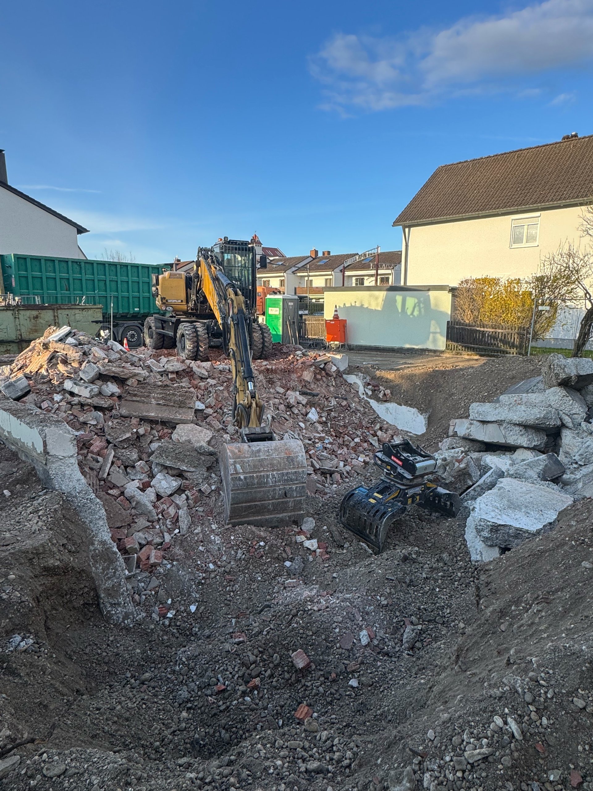Excavator working on construction site with rubble and debris, residential buildings in background