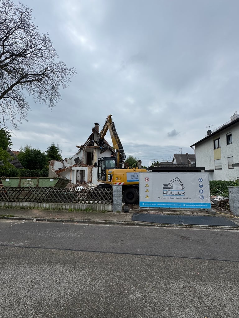 Yellow excavator demolishing a white house on a residential street under cloudy skies