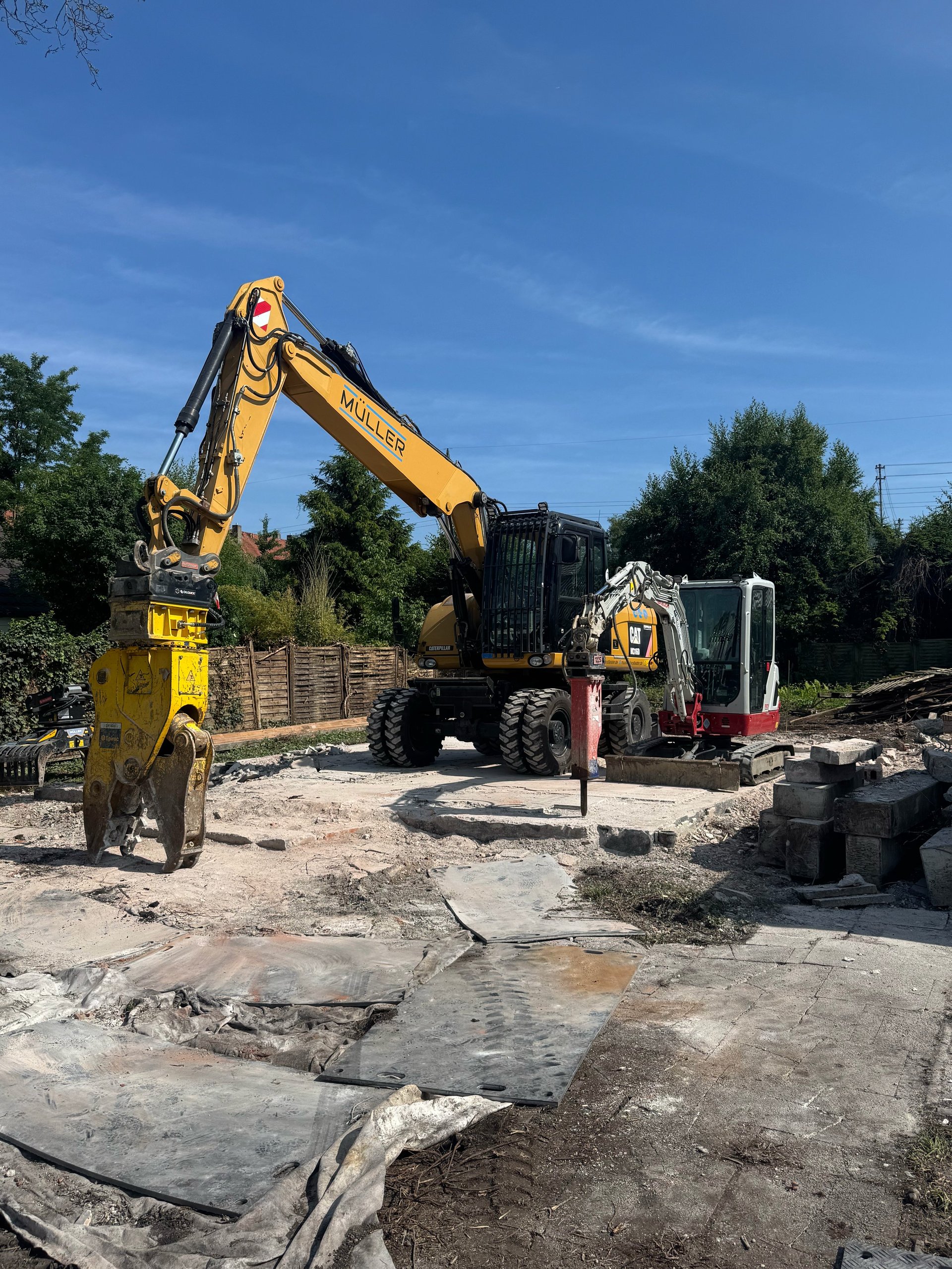 Yellow excavator on construction site with truck and equipment in background under blue sky