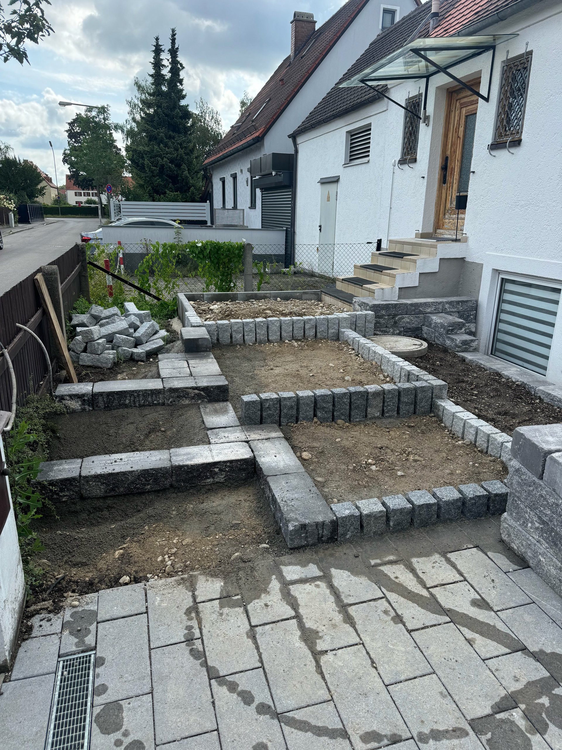 White house backyard with raised garden beds under construction, paved pathway, and landscaping in progress